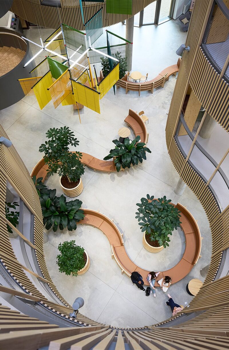 Moderne atrium med buede bænke, store planter og lyse, geometriske dekorationer.