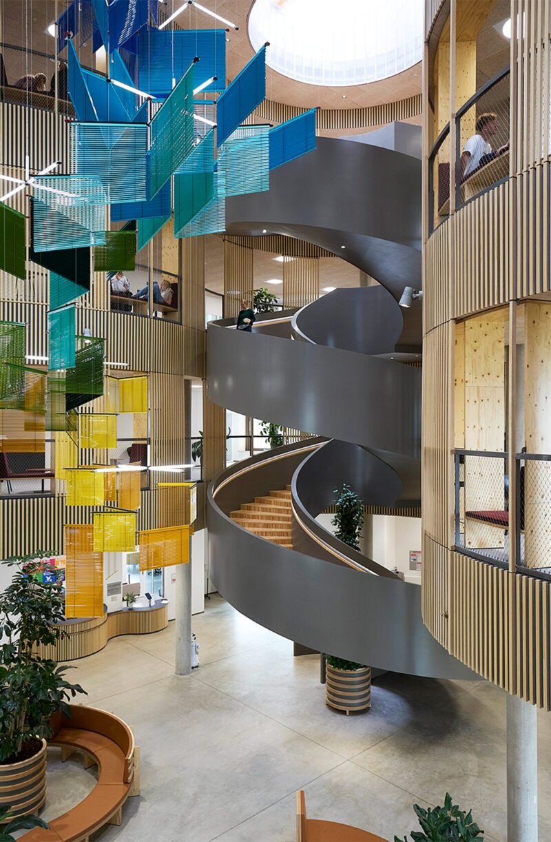 Indendørs moderne trappe og farverige glasplader i åbent, lyst kontormiljø.