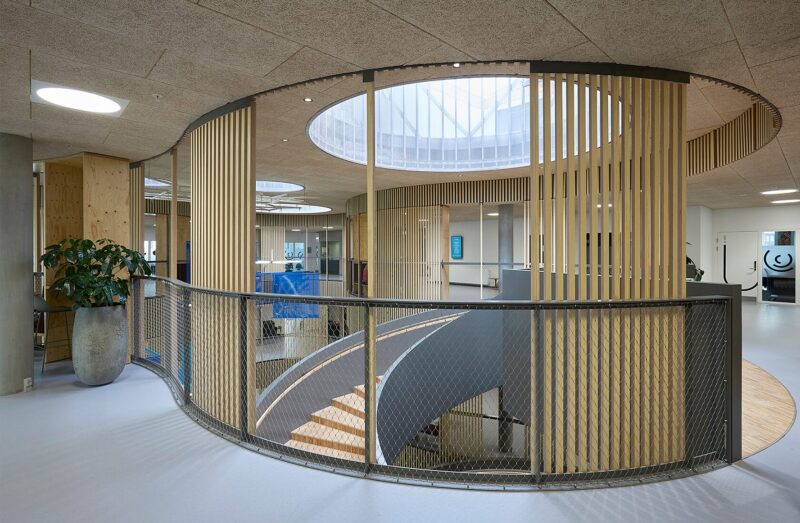 Moderne kontorbygning med runde trapper og træpaneler. Lys og rummelig arbejdsplads.