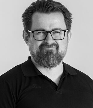 Portræt af person med briller og skæg i sort polo på grå baggrund