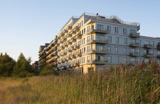 Moderne lejligheder ved solnedgang, omgivet af græs og træer.