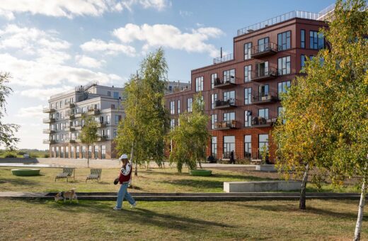 Kvindelig hundelufter går forbi moderne lejlighedskompleks på solrig dag.