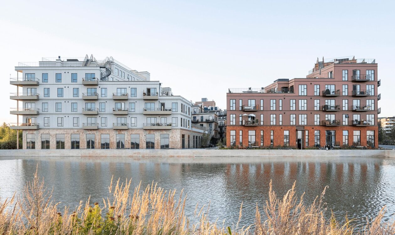 Moderne lejlighedsbygninger ved en vandkanal, med altaner og reflekterende vandoverflade.