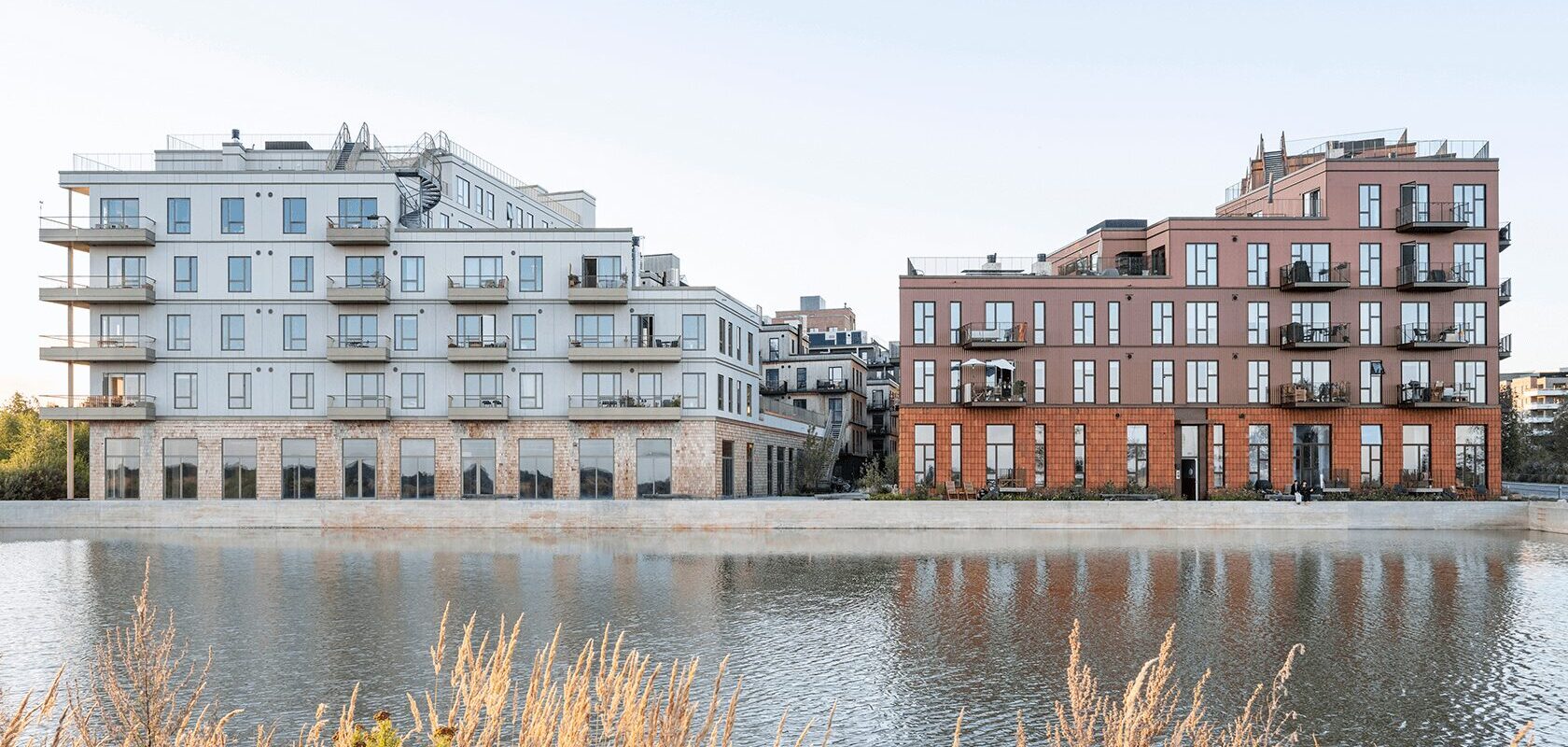 Moderne lejlighedsbygninger ved en vandkanal, med altaner og reflekterende vandoverflade.