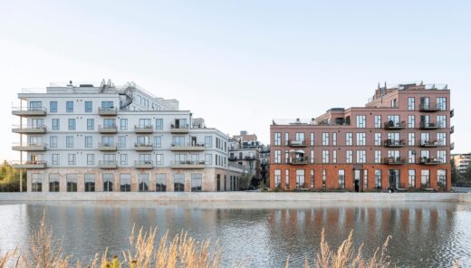 Moderne lejlighedsbygninger ved en vandkanal, med altaner og reflekterende vandoverflade.