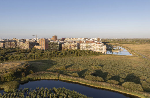 Moderne lejlighedsbygninger omgivet af naturreservat med sø og grønne områder under blå himmel.
