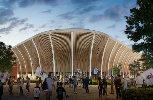 Ny stadion bygning med belysning, mennesker og flag i forgrunden, skumring himmel i baggrunden.