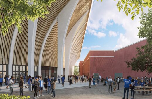 Folk samles foran moderne bygninger med buede tagkonstruktioner og røde vægge under en blå himmel.