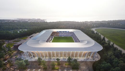 Modern football stadium surrounded by lush forest and crowd approaching.