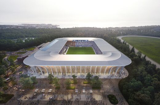 Modern football stadium surrounded by lush forest and crowd approaching.