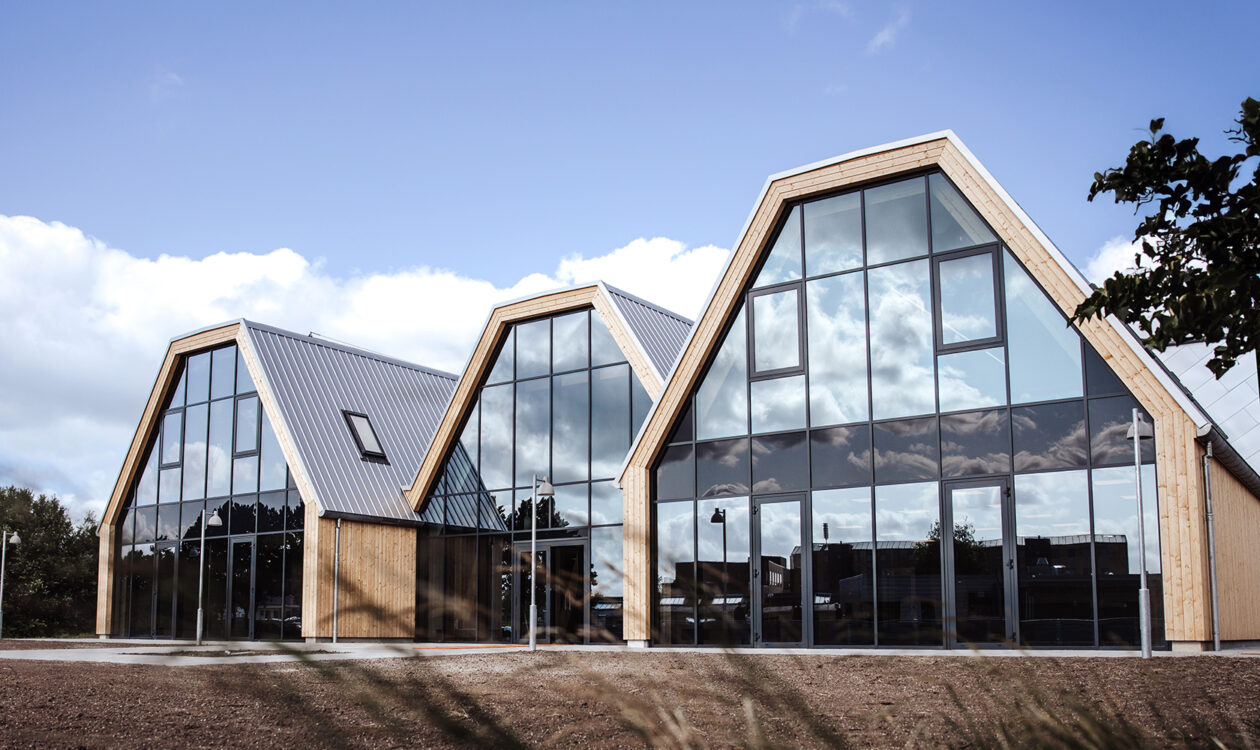 Ny moderne bygning med glasfacader og træbeklædning under en blå himmel.
