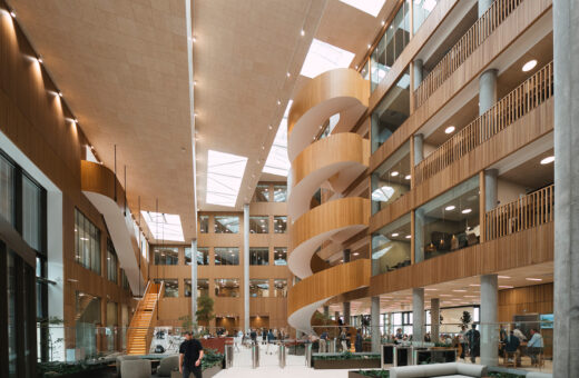 Moderne kontorbygning med træpaneler, glasvægge og spiraltrappe, mennesker arbejder og går rundt.