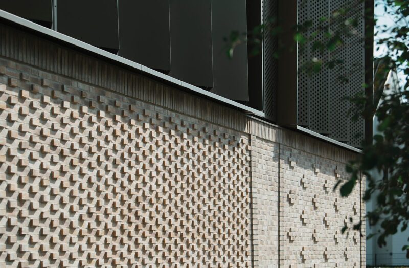 Mur med geometrisk mønster og mørke paneler på bygning i dagslys.
