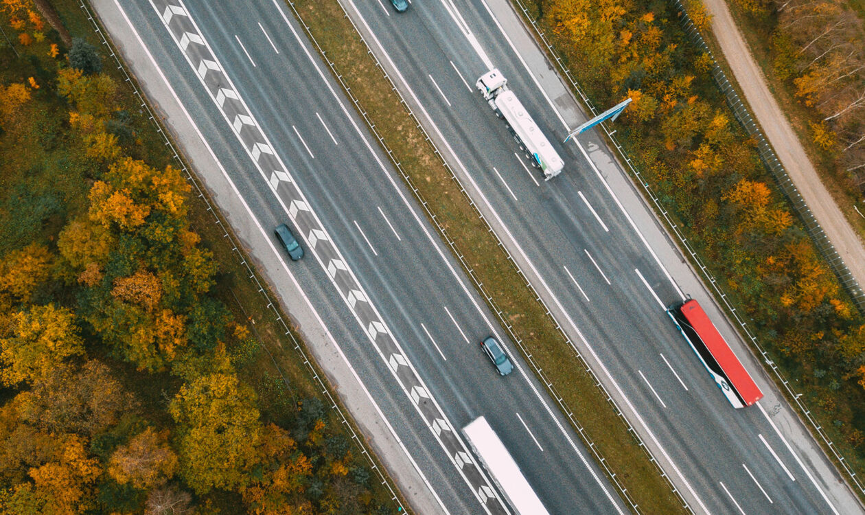 Luftfoto af motorvej med biler og lastbiler omgivet af efterårsfarvede træer.