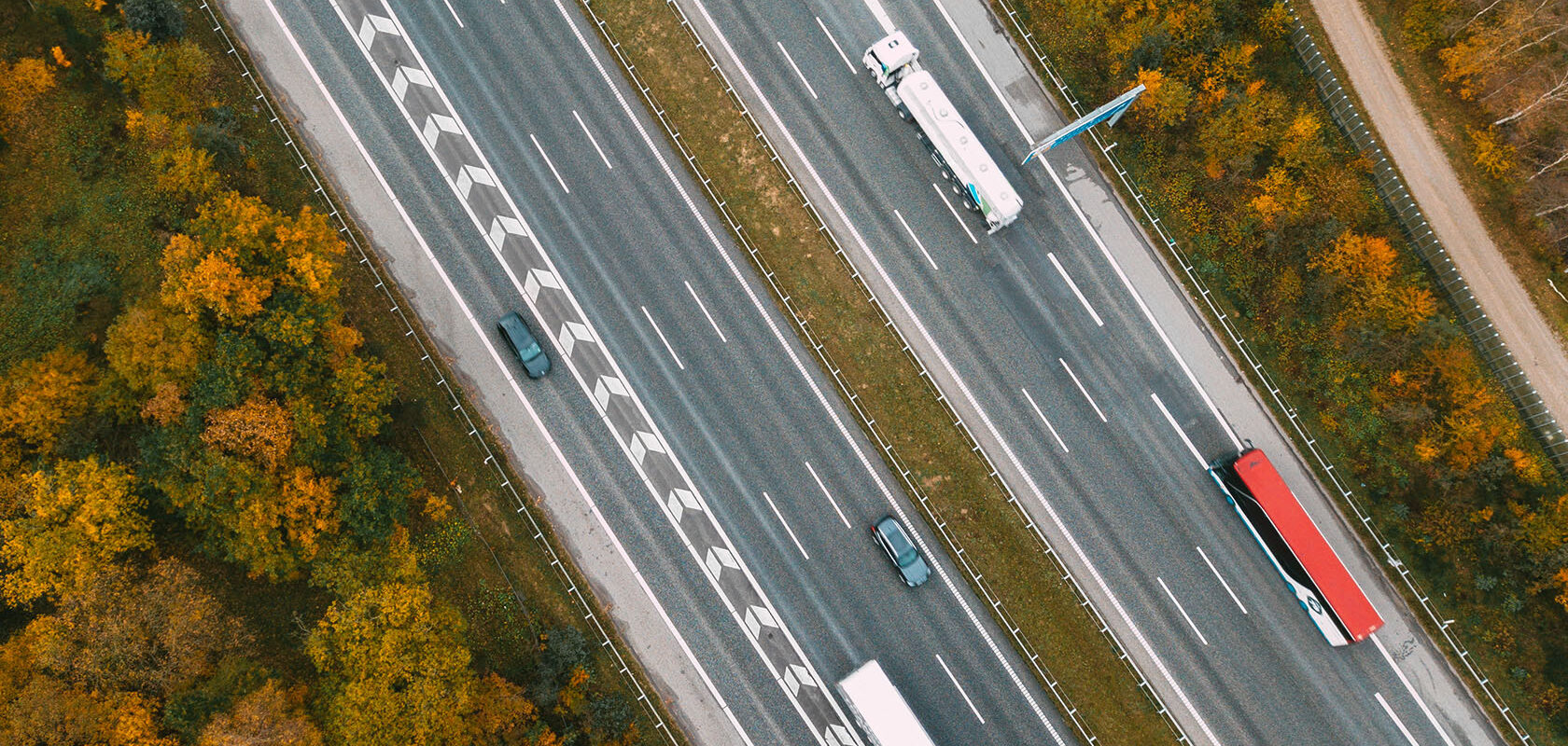 Luftfoto af motorvej med biler og lastbiler omgivet af efterårsfarvede træer.