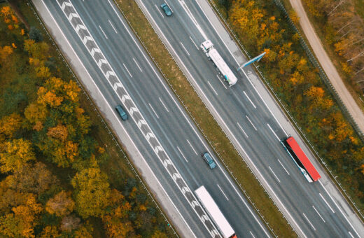 Luftfoto af motorvej med biler og lastbiler omgivet af efterårsfarvede træer.