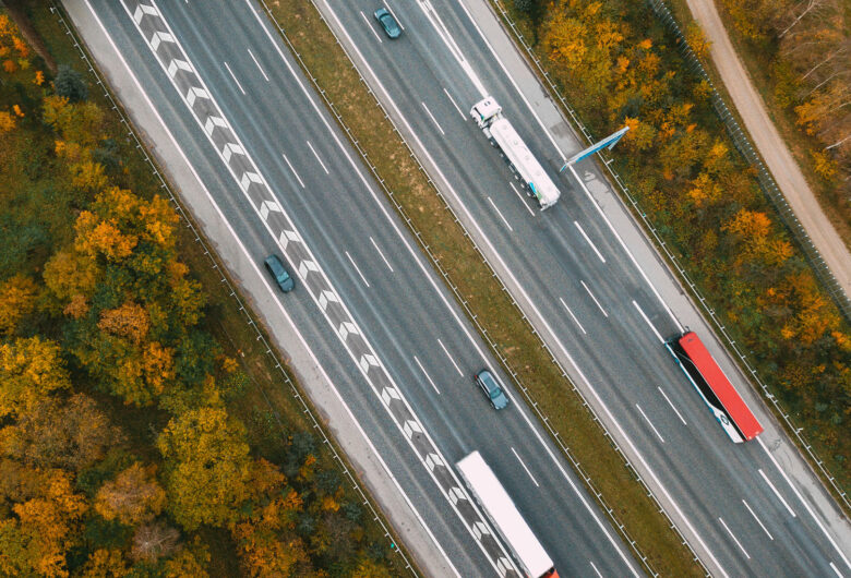 Luftfoto af motorvej med biler og lastbiler omgivet af efterårsfarvede træer.