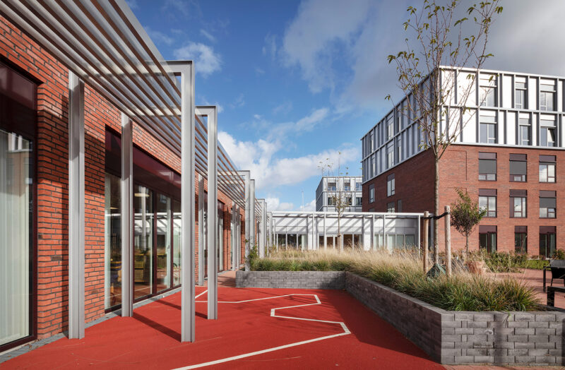 Moderne bygninger med rød mursten og metalarkitektur under blå himmel.