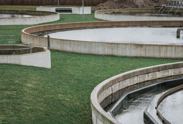 Afløbsanlæg med cirkulære bassiner til vandbehandling og græsarealer rundt omkring.