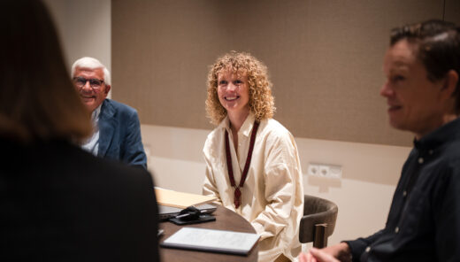 Fire personer i et mødelokale, to mænd og to kvinder, sidder ved et rundt bord under en samtale.