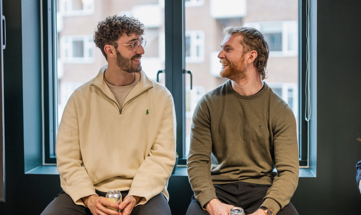 To mænd sidder ved vinduet og drikker dåsesodavand i en moderne bygning.