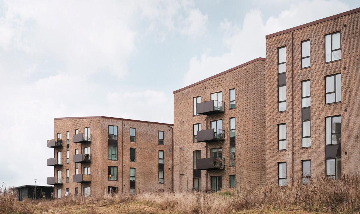 Moderne lejlighedsbygninger af teglsten med altaner ved et kæret område.