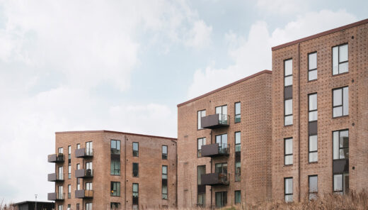 Moderne lejlighedsbygninger af teglsten med altaner ved et kæret område.