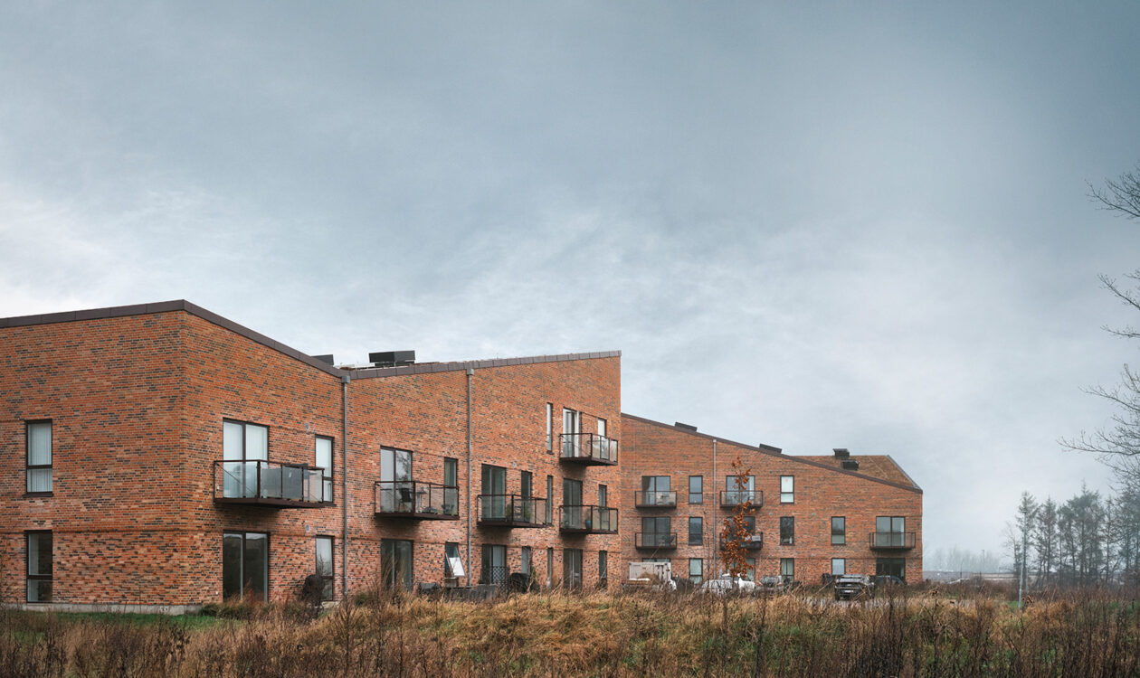 Moderne murstensbygninger med balkoner og græsarealer under overskyet himmel