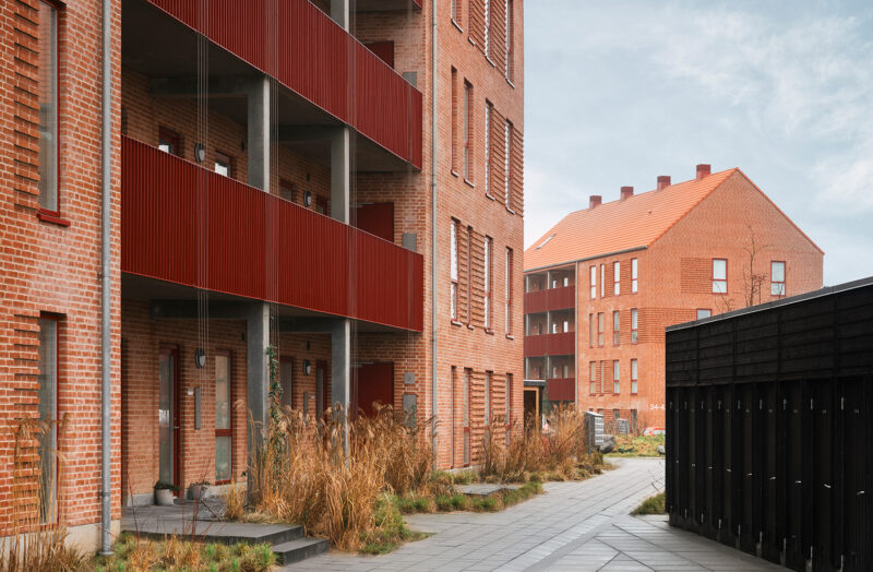 Nyt murstensbyggeri med røde altaner og moderne design. Gårdsplads med beplantning og gangstier.