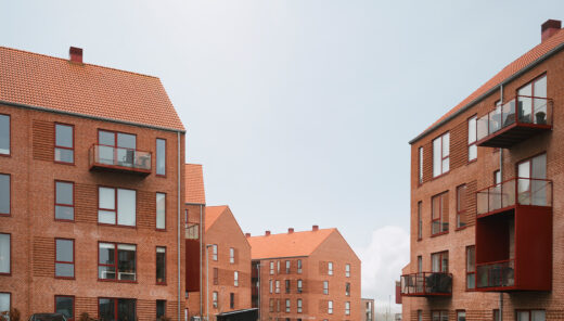 Røde murstensbygninger med altaner, parkeringsområde og biler i en moderne boligkompleks.