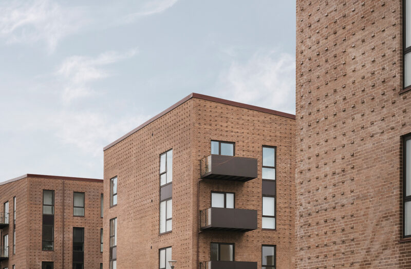 Moderne murstensbygninger med balkoner under en klar, blå himmel.