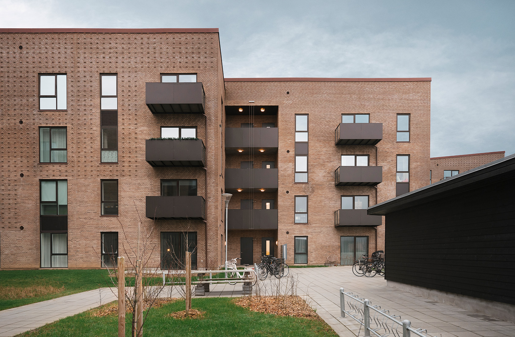 Moderne lejlighedskompleks i mursten med altaner og cykler parkeret udenfor.