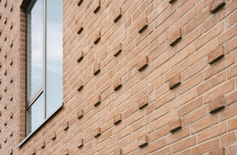 Mur med mønstret teglsten nær vindue. Moderne arkitektur med innovative detaljer.