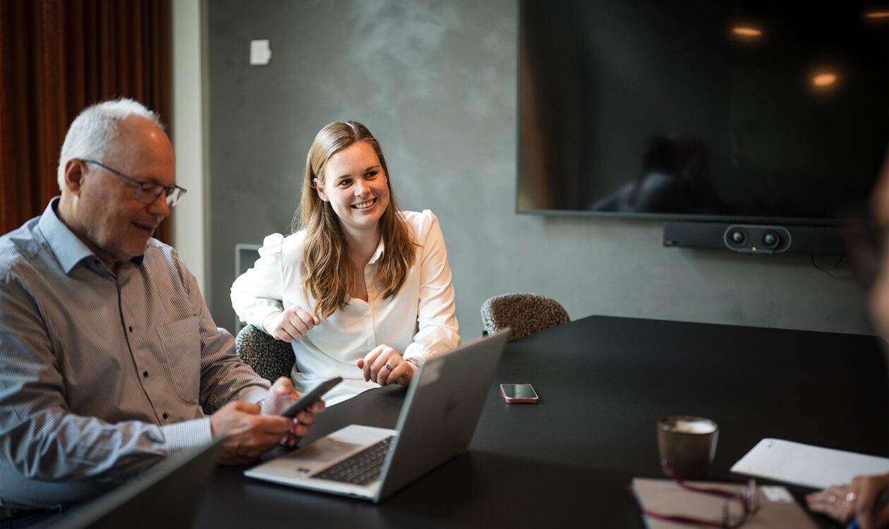 Forretningsmøde i mødelokale med bærbar computer, smartphone og stor skærm