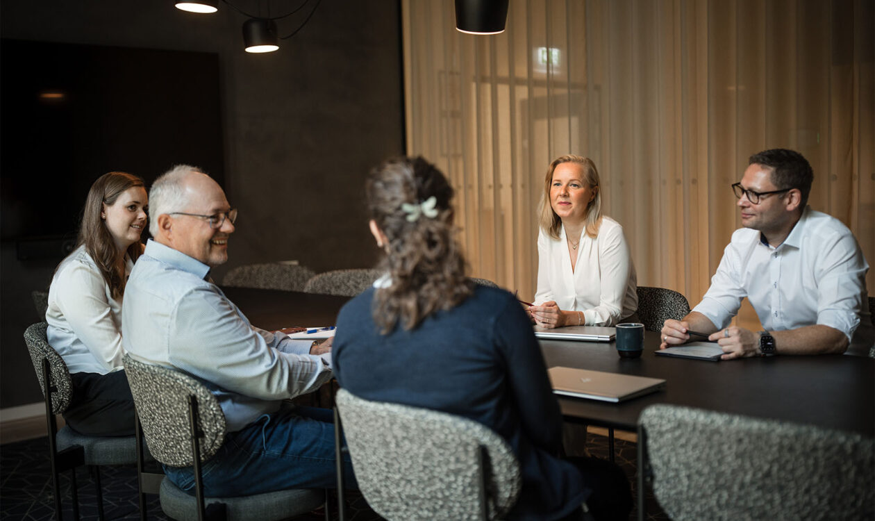 Forretningsmøde i moderne mødelokale med seks personer omkring konferencebord
