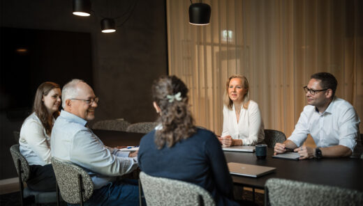 Forretningsmøde i moderne mødelokale med seks personer omkring konferencebord