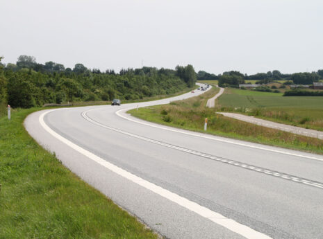 Snoet landevej gennem grønt dansk landskab med få biler og cykelsti ved siden af