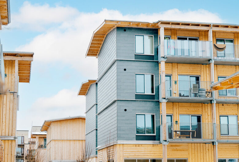 Moderne lejlighedsbygning med træ- og gråelementer, balkon og klar blålighimmel.