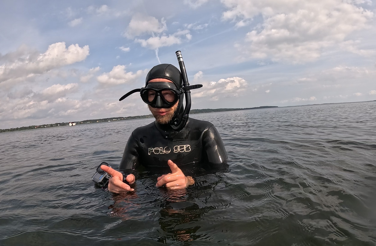 Snorkeldykker i sort våddragt står i havet under skyet himmel