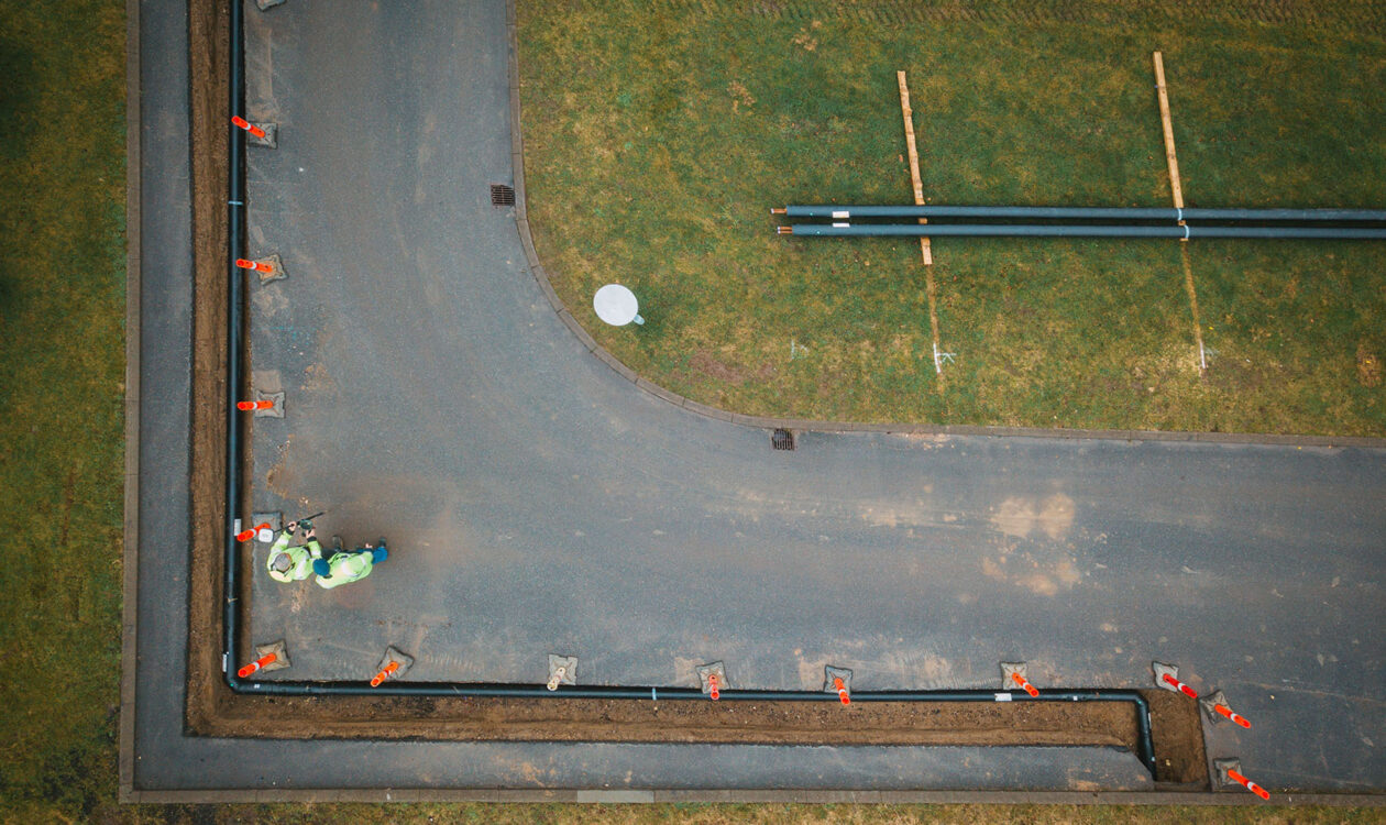 Luftfoto af vejarbejde med gravet rende, rør og to arbejdere i sikkerhedstøj